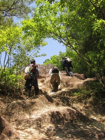 岩肌の露出した急斜面を登山参加者が登る様子を下から撮影