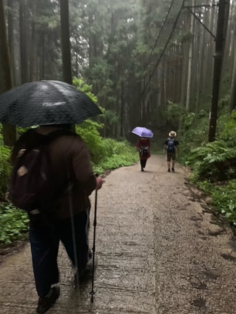 雨の中、坂道を降りていく3人の後ろ姿。